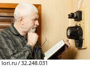 The man takes the readings of the apartment electric meter and writes it in the notebook. Стоковое фото, фотограф Акиньшин Владимир / Фотобанк Лори