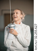 A young smiling woman fencer standing in the gym with a sword up and looking at it. Стоковое фото, фотограф Константин Шишкин / Фотобанк Лори