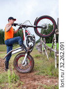 Fellow with trial mototrcycle training in countryside area, raising bike on rear wheel, leaning against wooden fence. Стоковое фото, фотограф Кекяляйнен Андрей / Фотобанк Лори