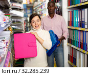 Portrait of happy woman demonstrating pink folder in stationary department of store. Стоковое фото, фотограф Яков Филимонов / Фотобанк Лори