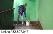 A young woman in blue jeans and a cage shirt swings and washes the floor on a staircase next to an elevator in a Stalinist-built apartment building, Cleaning public spaces by a labor immigrant cleane. Стоковое видео, видеограф Куликов Константин / Фотобанк Лори
