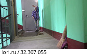 A young woman in blue jeans and a cage shirt swings and washes the floor on a staircase next to an elevator in a Stalinist-built apartment building, Cleaning public spaces by a labor immigrant cleane. Стоковое видео, видеограф Куликов Константин / Фотобанк Лори