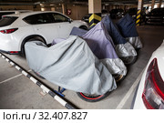 Motorcycles are parked on underground parking lot, covered with tents, standing between cars. Стоковое фото, фотограф Кекяляйнен Андрей / Фотобанк Лори