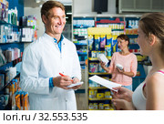 portrait of man druggist in white coat giving advice to customers in pharmacy. Стоковое фото, фотограф Яков Филимонов / Фотобанк Лори