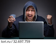 Young man wearing a hoodie sitting in front of a laptop computer. Стоковое фото, фотограф Elnur / Фотобанк Лори