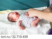 Loud crying baby with abdominal pain laying on bedsheet, human hands touching belly and calming. Стоковое фото, фотограф Кекяляйнен Андрей / Фотобанк Лори