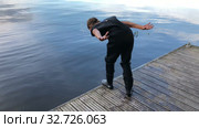 Young girl dressed wetsuit jumping in water from wooden pier, swimming in cold lake. Стоковое видео, видеограф Кекяляйнен Андрей / Фотобанк Лори