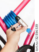 Human hand holding cable lock with integrated padlock for bicycle fastening to a fixed bike rack, white background. Стоковое фото, фотограф Кекяляйнен Андрей / Фотобанк Лори