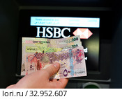 Doha, Qatar - Nov 17. 2019. Qatari rials in hand on the background of ATM of HSBC Bank. Редакционное фото, фотограф Володина Ольга / Фотобанк Лори