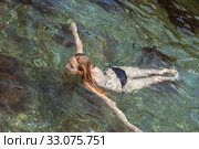 Beautiful slim young woman in a black bikini swimsuit resting on a rocky beach (2016 год). Стоковое фото, фотограф katalinks / Фотобанк Лори