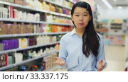 Portrait of cheerful young Asian woman behind counter demonstrating hair dye products. Стоковое видео, видеограф Яков Филимонов / Фотобанк Лори