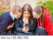 Russia Samara May 2019: three young girls with a smile look at the smartphone in a city park on a summer day. Редакционное фото, фотограф Акиньшин Владимир / Фотобанк Лори