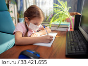 Girl schoolgirl in a medical mask does homework in front of a computer. Quarantine and distance learning. Стоковое фото, фотограф Екатерина Кузнецова / Фотобанк Лори