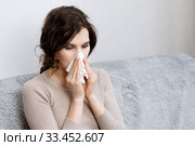 Sick woman suspected of covid-19 being at home in bed sneezes. Closeup sick girl sneezes in handkerchief Girl is quarantined with suspected coronavirus. Young woman sick in bed. Стоковое фото, фотограф Сергей Тимофеев / Фотобанк Лори