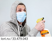 Scared man in hood with face mask cleaning with spray to protect him from Coronavirus. Covid-19 pandemic. Стоковое фото, фотограф Кекяляйнен Андрей / Фотобанк Лори