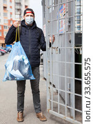 Adult Caucasian man wearing surgical mask taking out the garbage to trash enclosure of residential house. Стоковое фото, фотограф Кекяляйнен Андрей / Фотобанк Лори