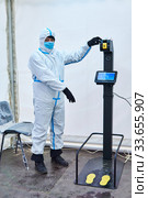 Medical officer invites to take non-contact temperature measurement in a tent of sanitary-epidemiological control in Perm, Russia (2020 год). Редакционное фото, фотограф Евгений Харитонов / Фотобанк Лори