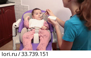 Teenage girl feeding her sister with teaspoon with additional food, first eating with complementary foods. Стоковое видео, видеограф Кекяляйнен Андрей / Фотобанк Лори