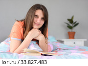 Девушка читает книгу лежа на кровати в комнате и отвлеченно посмотрела в окно. Стоковое фото, фотограф Иванов Алексей / Фотобанк Лори