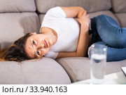 Mexican female at sofa holding hands on the illness stomache. Стоковое фото, фотограф Яков Филимонов / Фотобанк Лори