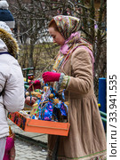 Moscow, Russia, February 2020. A girl in an old national costume sells Souvenirs for Maslenitsa. Редакционное фото, фотограф Artem Sobov / Фотобанк Лори