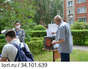 Мужчина опускает в переносную урну бюллетень. Досрочное голосование по внесению поправок в конституцию Российской Федерации, 2020 год. Временный избирательный пункт во дворе жилого дома. Калининград. Редакционное фото, фотограф Ирина Борсученко / Фотобанк Лори