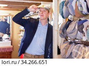 man try on trilby hat and looking at mirror in headwear shop. Стоковое фото, фотограф Яков Филимонов / Фотобанк Лори