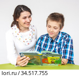 A boy and a woman sit at a table looking through a book, they like the content and they smile  Семья, мать, и сын сидят за столом читают книгу, делятся впечатлениями от прочитанного или иллюстрации, производится обучение. Стоковое фото, фотограф Владимир Ушаров / Фотобанк Лори