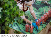 Продавщица выкладывает на прилавока стаканчики с нарезанными кусочками арбуза для продажи у фонтана в магазине ГУМ в центре города Москвы, Россия (2020 год). Редакционное фото, фотограф Николай Винокуров / Фотобанк Лори