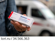 Волонтер держит коробку с тривалентной вакциной "Гриппол Плюс" на фоне специального автомобиля скорой помощи мобильного пункта бесплатной вакцинации от гриппа на Тверской улице у метро в центре города Москвы, Россия (2020 год). Редакционное фото, фотограф Николай Винокуров / Фотобанк Лори