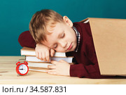 tired school boy asleep on books. little student sleeping on textbooks. Child in school uniform lies on the table with big pile of books against blue wall. Eyes closed. School concept. Стоковое фото, фотограф Nataliia Zhekova / Фотобанк Лори