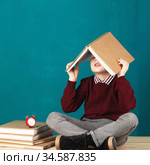 Cheerful smiling little school boy with big books on his head having fun against turquoise wall. Стоковое фото, фотограф Nataliia Zhekova / Фотобанк Лори