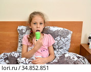 Больная девочка держит в руке спрей и орошает им горло, лежа в постели. Самолечение. Стоковое фото, фотограф Ирина Борсученко / Фотобанк Лори