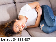 Mexican female at sofa holding hands on the illness stomache. Стоковое фото, фотограф Яков Филимонов / Фотобанк Лори