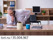 Old male employee suffering from radiculitis at workplace. Стоковое фото, фотограф Elnur / Фотобанк Лори