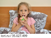 Девочка держит в руках спрей и орошает им горло, сидя в постели. Самолечение. Стоковое фото, фотограф Ирина Борсученко / Фотобанк Лори