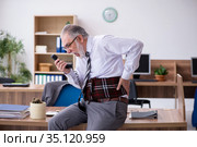 Old male employee suffering from radiculitis at workplace. Стоковое фото, фотограф Elnur / Фотобанк Лори