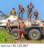 Russia, Samara, June 2019: young athletic people, participants in the hero race, climb through an armored personnel carrier in the village of Roshchinsky near Samara. Text in Russian: race of heroes, platoon. Редакционное фото, фотограф Акиньшин Владимир / Фотобанк Лори