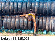 Russia, Samara, June 2019: athletic youth participates in a race of heroes and overcomes obstacles car tires on a summer day in the village of Roshchinsky . Text in Russian: race of heroes, platoon. Редакционное фото, фотограф Акиньшин Владимир / Фотобанк Лори