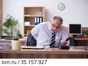 Old male employee suffering from radiculitis at workplace. Стоковое фото, фотограф Elnur / Фотобанк Лори