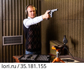 Man aiming smallbore sporting pistol at target in shooting range. Стоковое фото, фотограф Яков Филимонов / Фотобанк Лори
