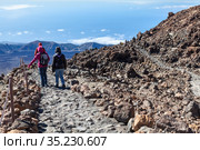 A group of tourists descend from the summit of the Teide volcano along a stone staircase among the lava heap. Three people in windproof clothes hiking. Tenerife Island, Canary Islands, Spain. Стоковое фото, фотограф Кекяляйнен Андрей / Фотобанк Лори