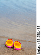 Детские розовые сабо стоят на песчаном пляже около воды. Children's pink clogs stand on a sandy beach near the water. Стоковое фото, фотограф Мария / Фотобанк Лори