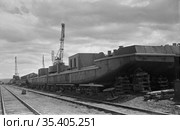 Железная дорога на территории речной гавани, корпус морской баржи установлен на деревянной подставке, стрелы подъёмных кранов на заднем плане, Осетрово, Чукотка, 1963 год. Стоковое фото, фотограф Варфоломей Тетерин / Фотобанк Лори
