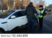 Инспектор дорожно-патрульной службы полиции проверяет документы водителя остановленного автомобиля (2016 год). Редакционное фото, фотограф Free Wind / Фотобанк Лори
