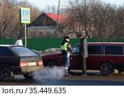 Инспектор дорожно-патрульной службы полиции проверяет документы водителя остановленного автомобиля (2016 год). Редакционное фото, фотограф Free Wind / Фотобанк Лори