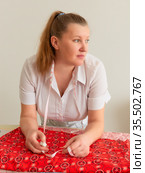 The woman is leaning over the table on which the cloth is lying, with a thoughtful look, holding a crayon and a tailor's meter. Женщина склонилась над столом, на котором лежит ткань, с задумчивым видом, держит мелок и портняжный метр. Стоковое фото, фотограф Владимир Ушаров / Фотобанк Лори