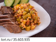 Булгур с овощами и мясом крупным планом. Гарнир из тушеных цукини с перловой крупой и помидорами. Порция питательного, здорового и аппетитного ужина на белом блюде. Ужин из запеченного нежирного мяса и сезонных овощей. bulgur with vegetables and meat close-up. Стоковое фото, фотограф Юлия Михайлова / Фотобанк Лори