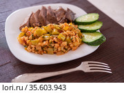 Гарнир из тушеных цукини с перловой крупой и помидорами крупным планом. Порция питательного, здорового и аппетитного ужина на белом блюде. Ужин из запеченного нежирного мяса и сезонных овощей. Closeup side dish of stewed zucchini with pearl barley and tomato. A serving of nutritious, healthy and mouth-watering dinner on a white dish. A dinner of baked lean meat and seasonal vegetables. Стоковое фото, фотограф Юлия Михайлова / Фотобанк Лори