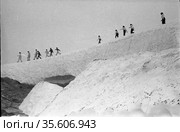 Вид снизу на людей шагающих друг за другом по леднику, взрослые люди и дети школьного возраста идут по льду, Чукотка, 1970 год. Редакционное фото, фотограф Варфоломей Тетерин / Фотобанк Лори